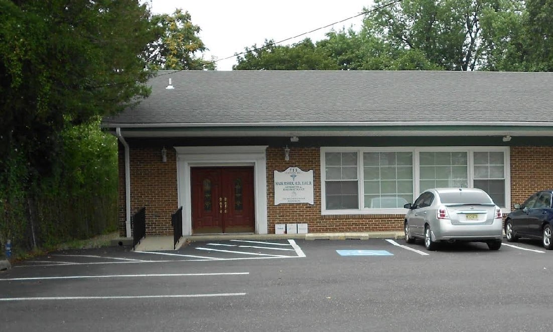 A brick building with a sloped roof, featuring a sign and two parked cars in a lot.