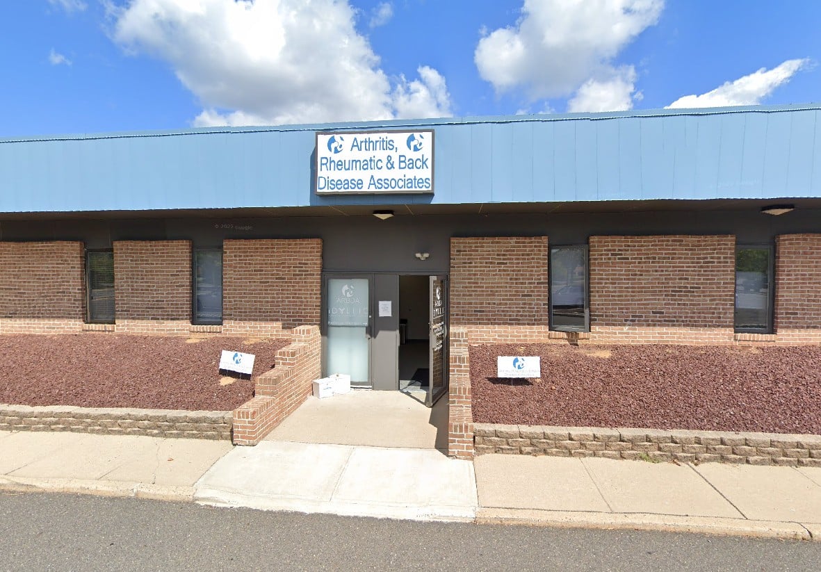 Exterior view of a medical building, 'Arthritis, Rheumatic & Back Disease Associates,' with a blue roof and brick walls.