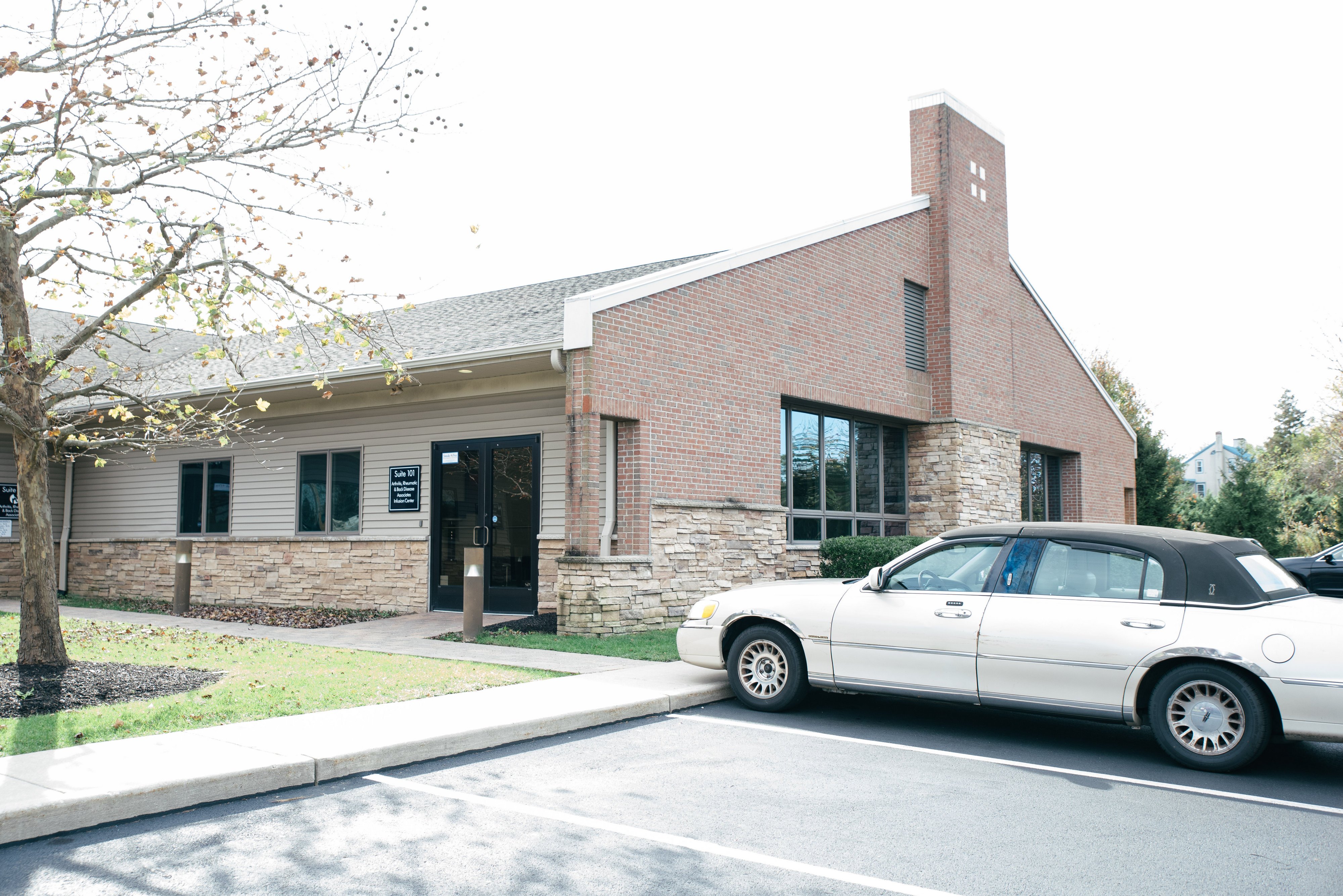 A brick building with large windows, surrounded by a grassy area and several parked cars under a clear sky.
