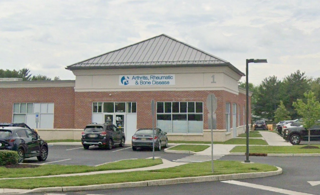 A building with a sign reading 'Arthritis, Rheumatic & Bone Disease' outside, surrounded by parked cars.