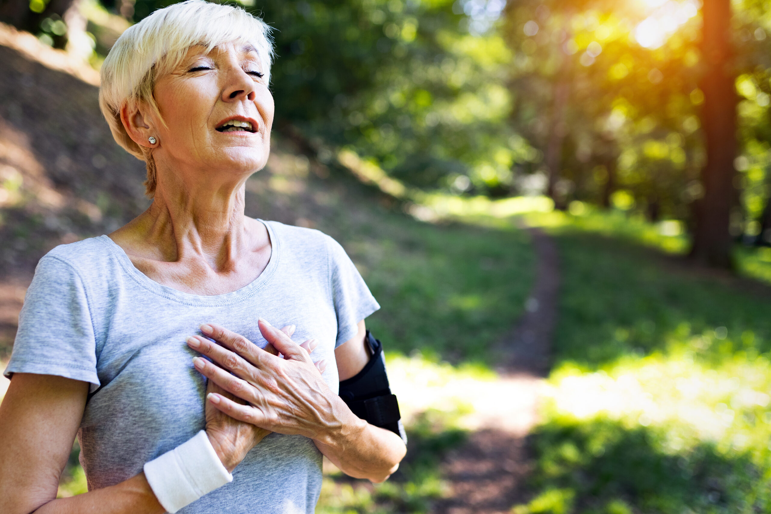 Older woman with asthma holding her heart as she exercises outdoors.
