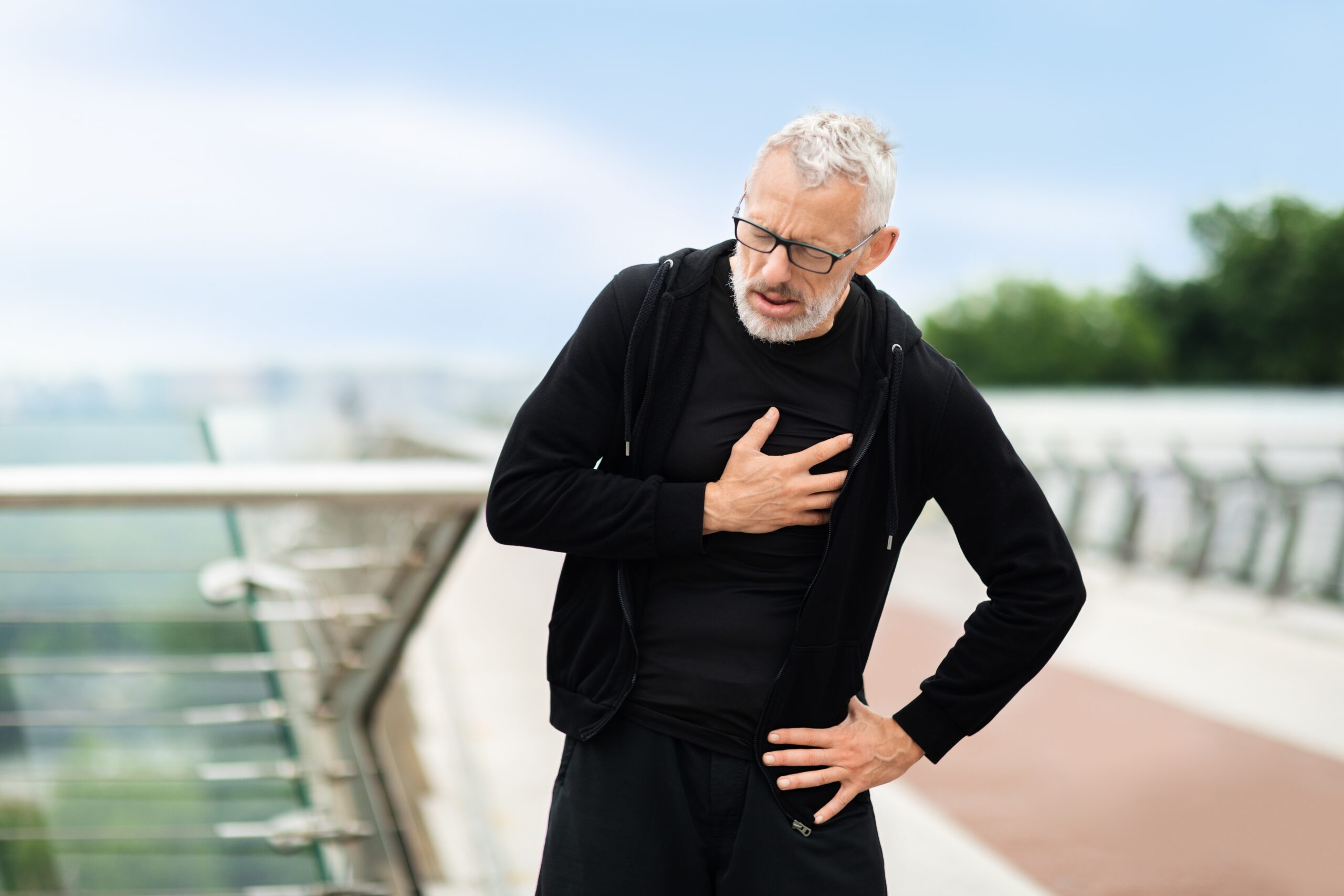 Man with rheumatoid arthritis holding his heart as he stops during his run.
