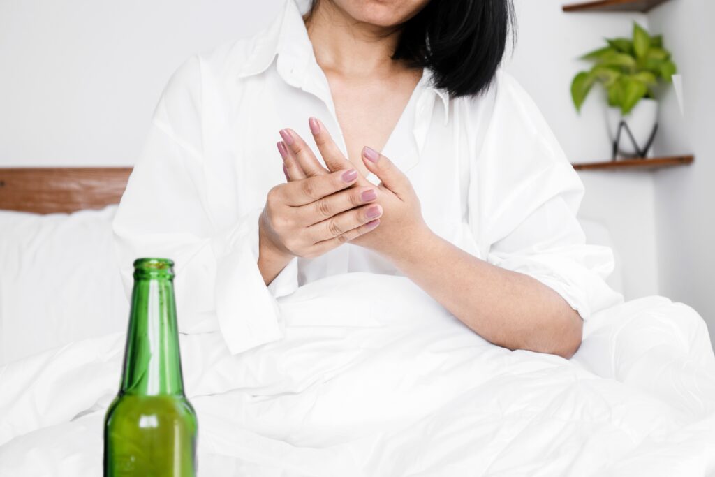 Woman holding hand while experiencing gout flare-up after drinking beer.