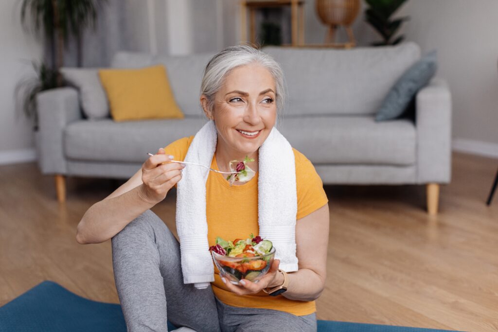 Older woman sitting on her workout mat eating a healthy salad.