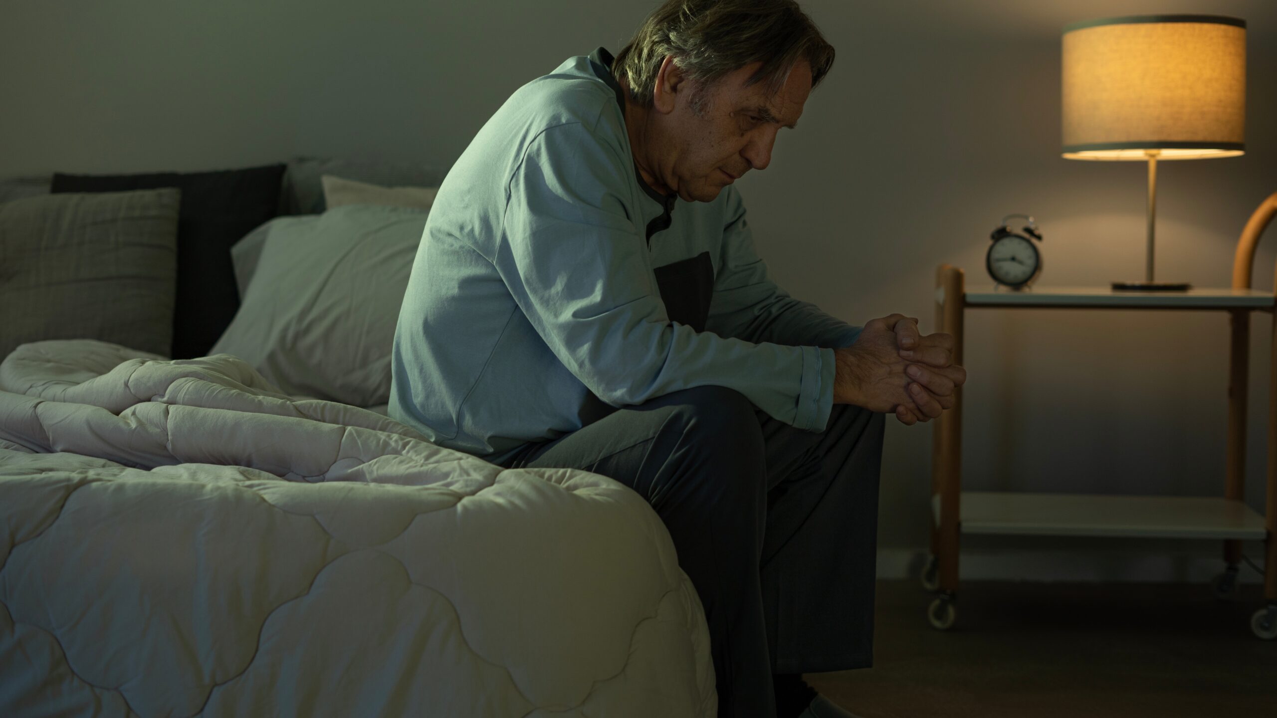 Elderly man with rheumatic condition sitting in bed late at night because he can't sleep.